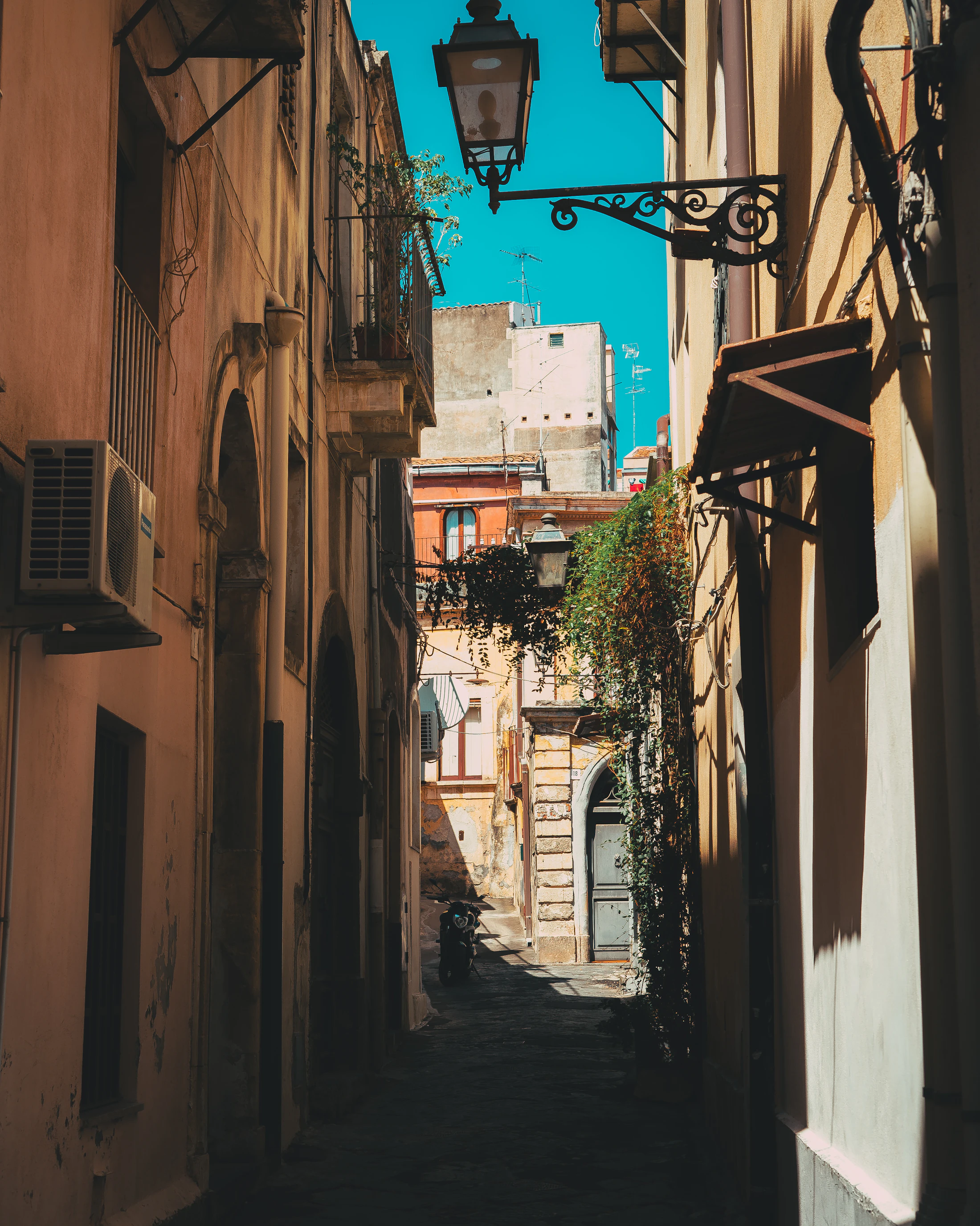 A sunlit lane between old buildings in Acireale